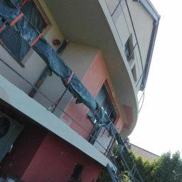 Remonty i wykończenia Oliwier Gacmenga - Budynek z częściowo ocieploną elewacją, okna zabezpieczone folią, widoczna drabina i wiaderka z farbą, budynek w trakcie prac remontowych.