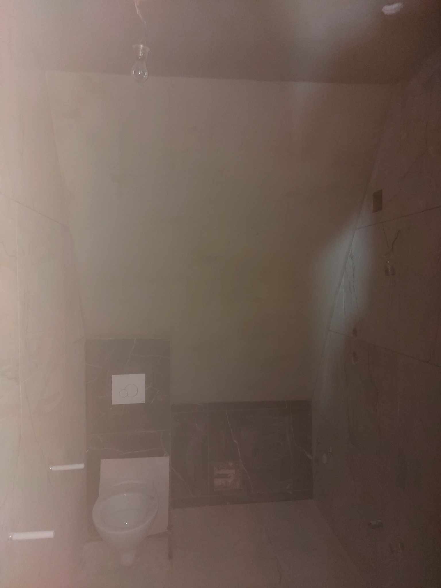 Niedokończona łazienka w Bytomiu z widoczną toaletą, płytkami imitującymi marmur i surową gładzią na ścianach pod skosem.