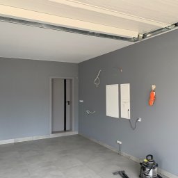 Wojciech Wałek - Szare wnętrze pokoju po malowaniu ścian i ułożeniu szarych płytek podłogowych, widoczne niedokończone instalacje elektryczne i odkurzacz przemysłowy.