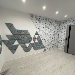 Wojciech Wałek - Pokój po remoncie z tapetą w dziecięce motywy samochodów, ścianą z trójkątnych paneli akustycznych w odcieniach szarości i bieli oraz szarą ościeżnicą drzwi.