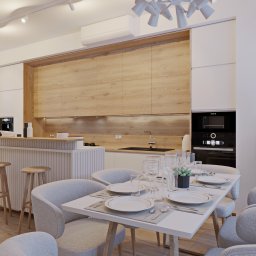 Yurii Fedenko Solutions - Nowoczesna kuchnia z drewnianymi frontami szafek górnych, białymi szafkami dolnymi, wyspą z hokerami i stołem jadalnym z nakryciem dla czterech osób. W tle widoczny czarny piekarnik i dekoracyjny...