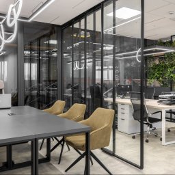Yurii Fedenko Solutions - Nowoczesne biuro z przeszklonymi ścianami, szarym stołem konferencyjnym, beżowymi krzesłami, wiszącymi lampami o abstrakcyjnym kształcie i ścianą z zielonych roślin.