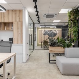 Yurii Fedenko Solutions - Nowoczesne biuro z drewnianymi akcentami, roślinami doniczkowymi i szklanymi ścianami, oświetlone reflektorami i lampami LED, z widoczną mapą Ukrainy podświetloną neonem w tle.