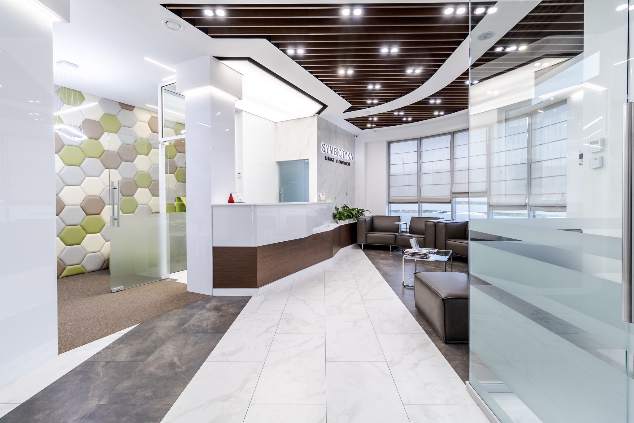 Nowoczesne wnętrze biura: biała recepcja z drewnianym akcentem, marmurowa podłoga, heksagonalna ściana i strefa oczekiwania z skórzanymi sofami.