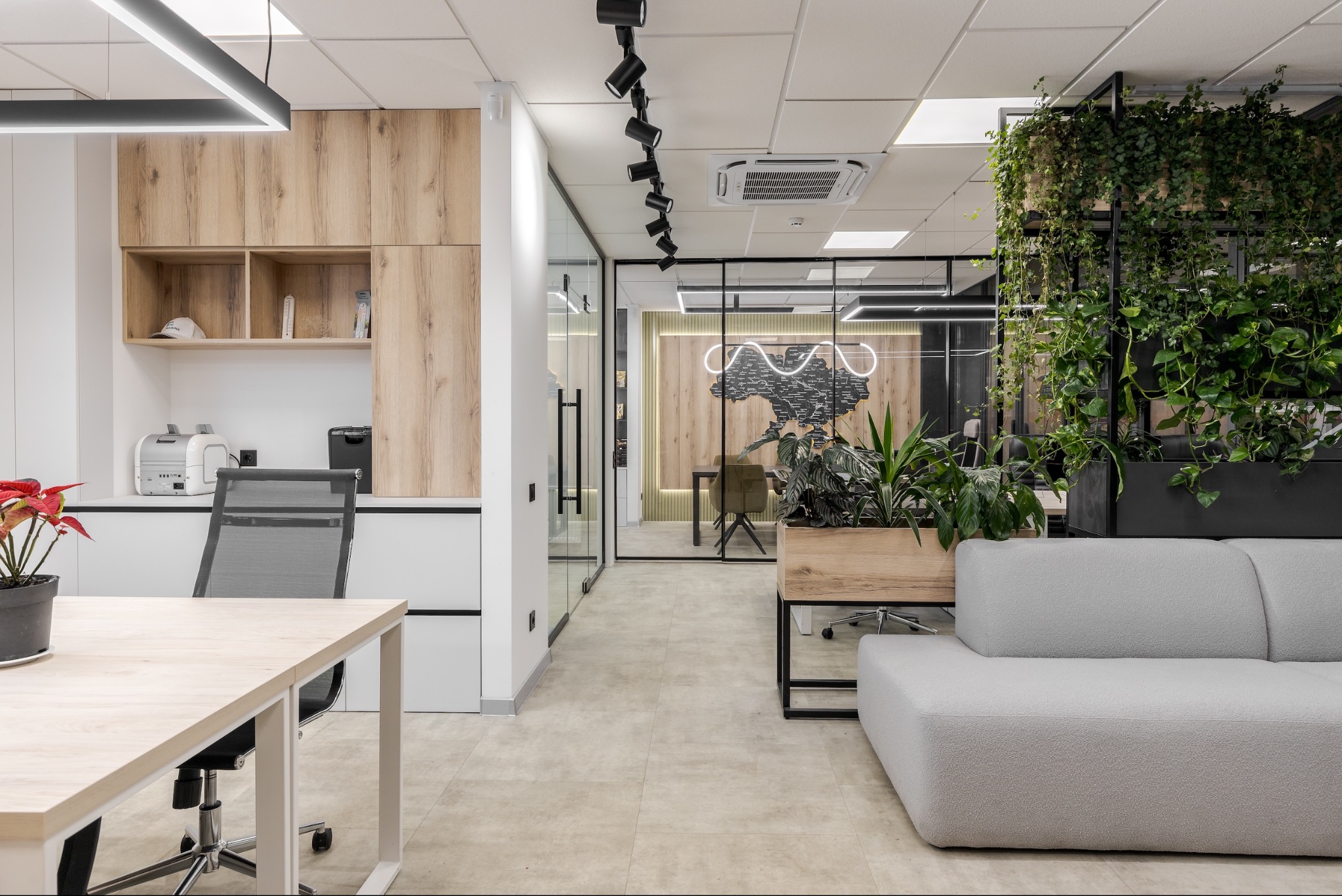 Nowoczesne biuro z drewnianymi akcentami, roślinami doniczkowymi i szklanymi ścianami, oświetlone reflektorami i lampami LED, z widoczną mapą Ukrainy podświetloną neonem w tle.