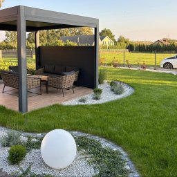 Ogrody Wojtala - Nowoczesny ogród z pergolą, meblami ogrodowymi i oświetleniem kulistym. Starannie utrzymany trawnik, obrzeża z kamienia i rośliny ozdobne tworzą harmonijną całość.