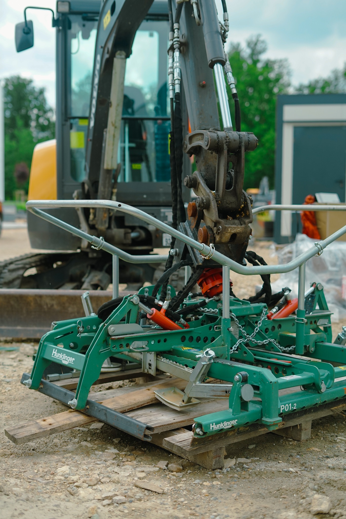 Chwytak próżniowy Hunklinger P01-2 zamontowany na ramieniu koparki, gotowy do podnoszenia kostki brukowej. Widoczne przewody hydrauliczne i elementy mocujące.