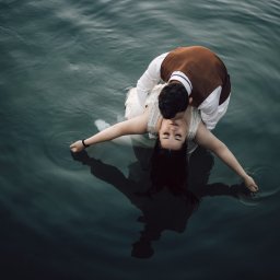 Zatrzymać Chwile - Para młoda w wodzie w Stargardzie: panna młoda w sukni z rozłożonymi ramionami, pan młody w brązowej kamizelce całuje ją w szyję, widok z góry na ciemną wodę.