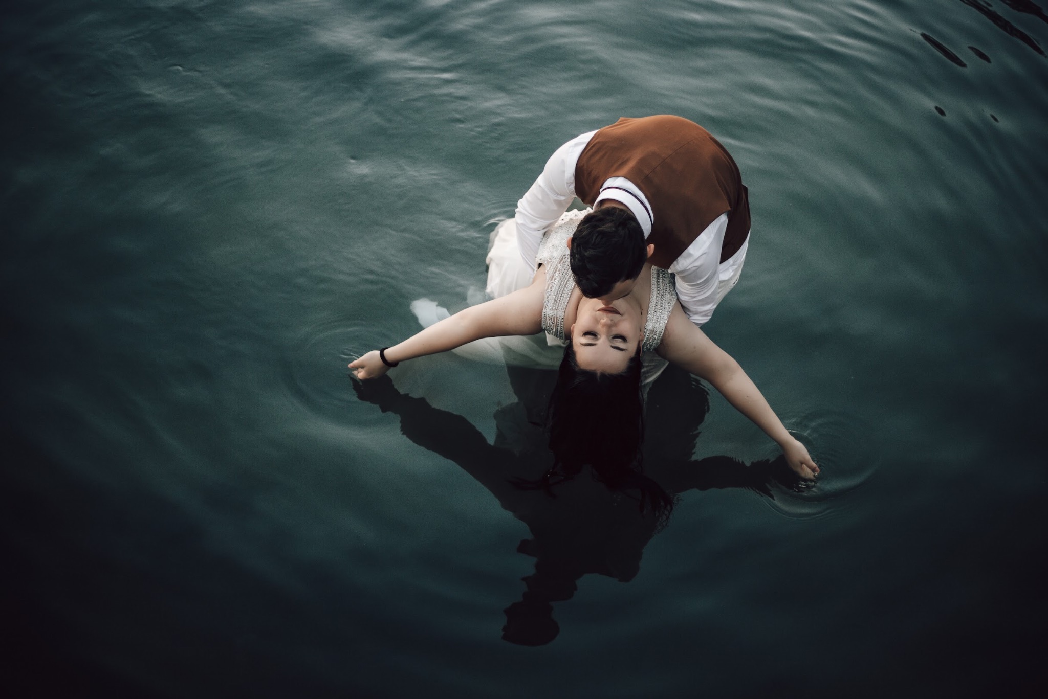 Para młoda w wodzie w Stargardzie: panna młoda w sukni z rozłożonymi ramionami, pan młody w brązowej kamizelce całuje ją w szyję, widok z góry na ciemną wodę.