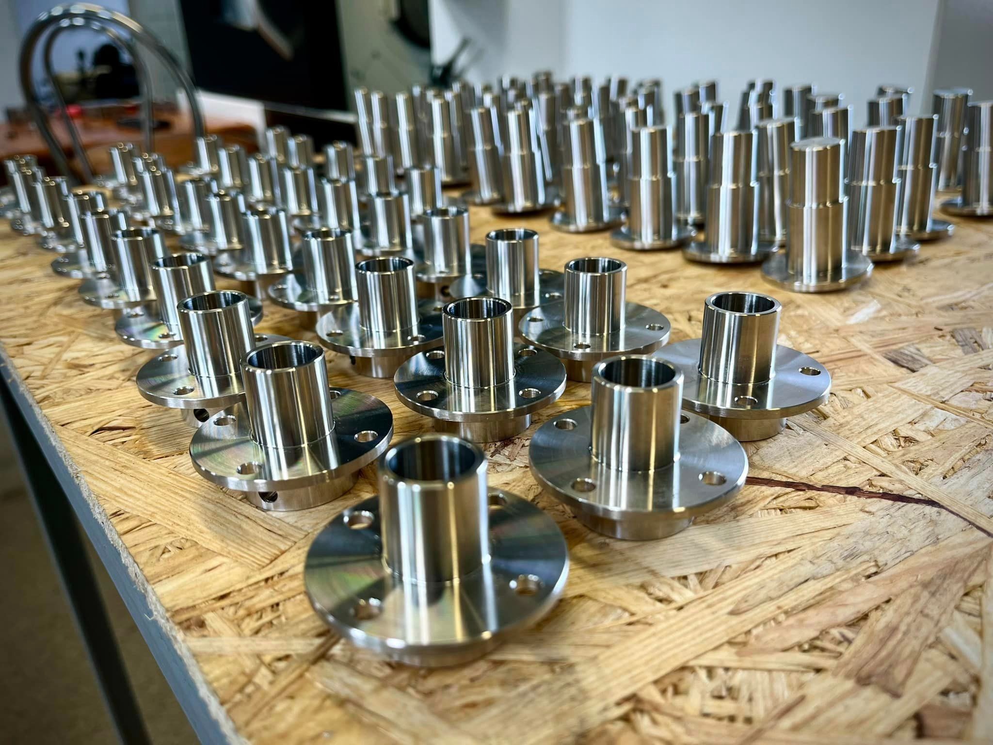 Rząd precyzyjnie wykonanych, metalowych kołnierzy z tulejami, ułożonych na płycie OSB, widok z góry, podkreślający powtarzalność i jakość wykonania.