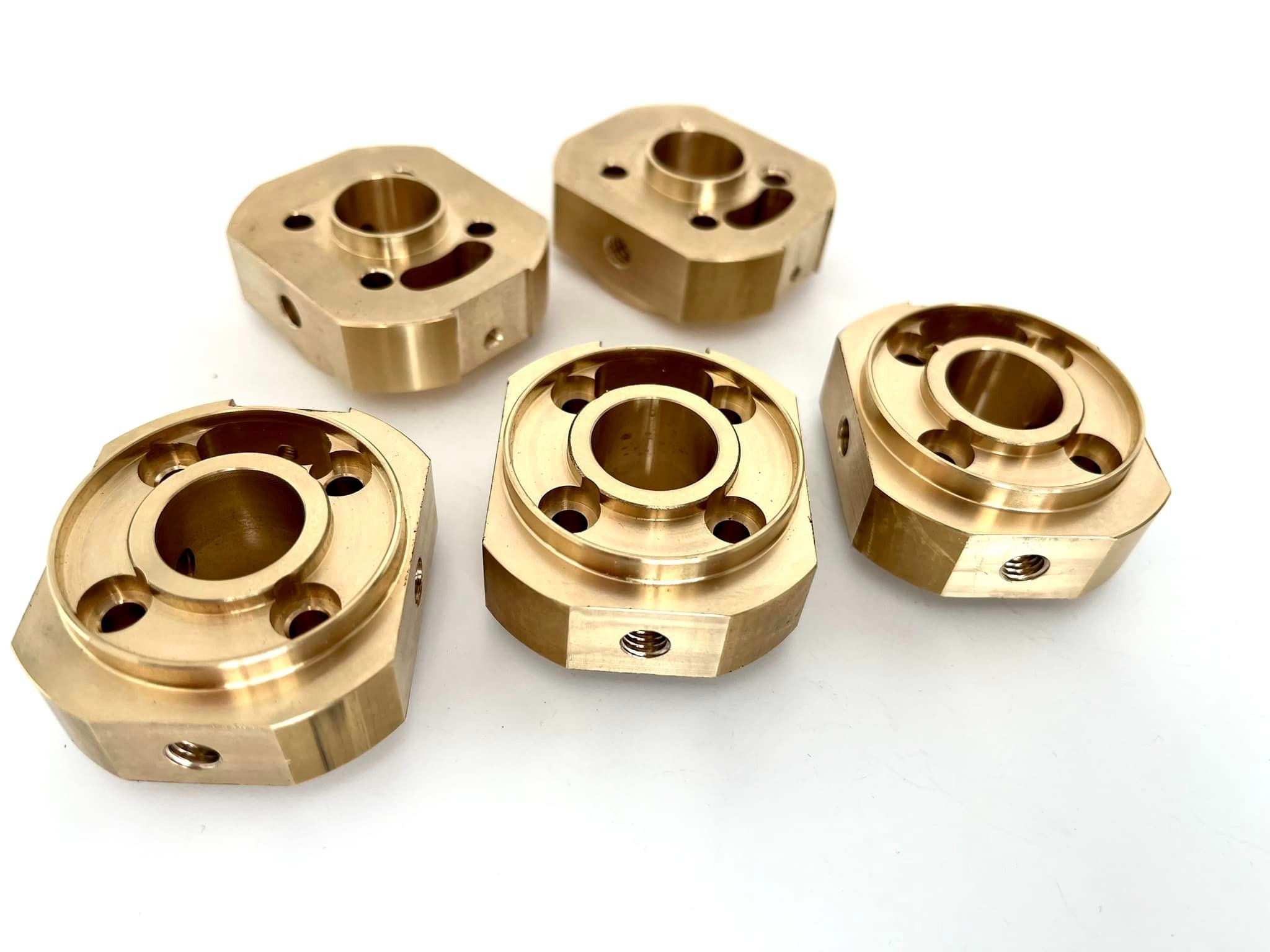 Pięć precyzyjnie wykonanych, złotych elementów metalowych z otworami, ułożonych na białym tle. Widoczne ślady obróbki mechanicznej i gwintowane otwory.