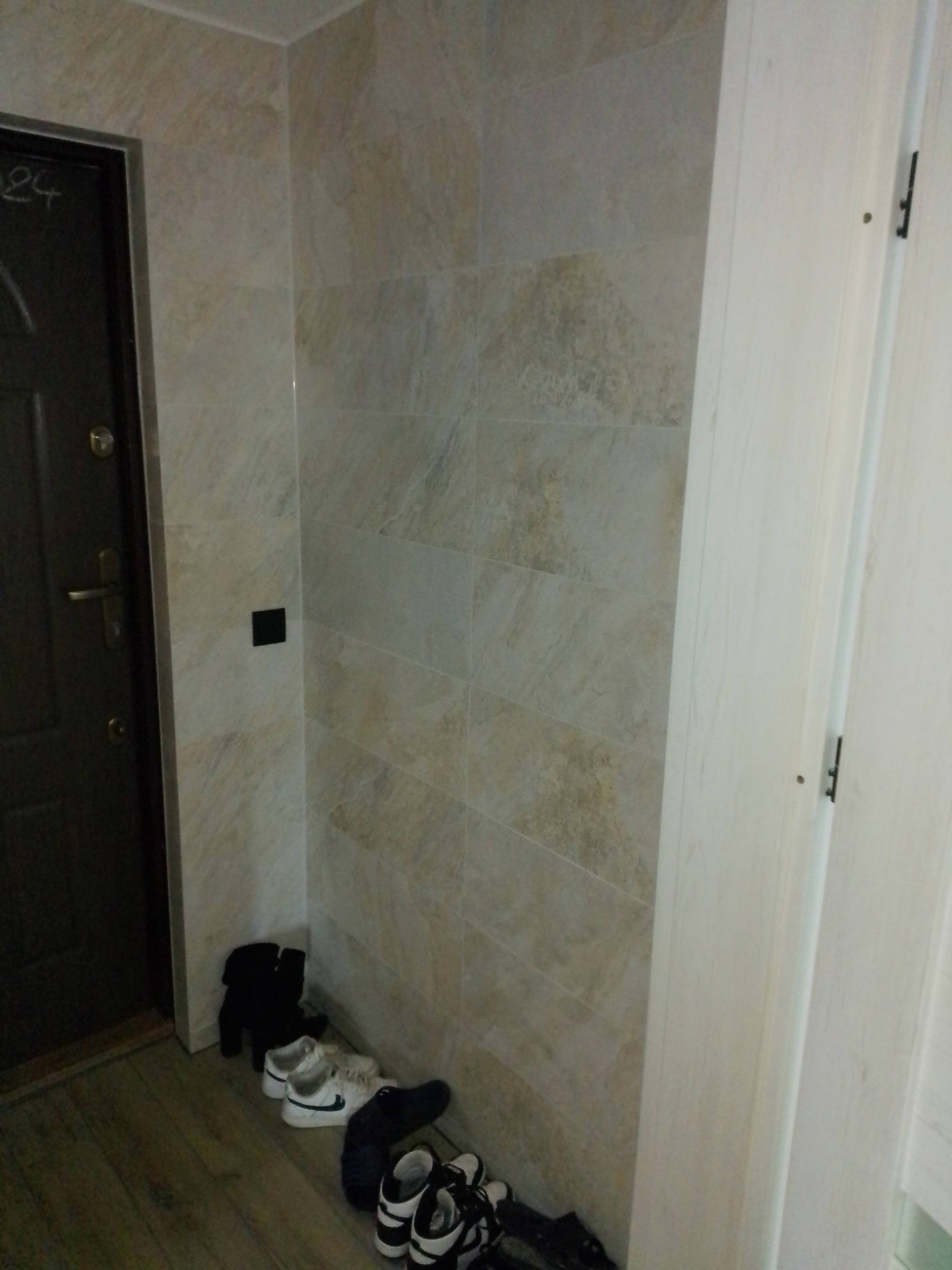 Kafelki imitujące kamień na ścianie w przedpokoju, widoczna część drzwi wejściowych i drzwi wewnętrznych, na podłodze panele i porozrzucane buty.