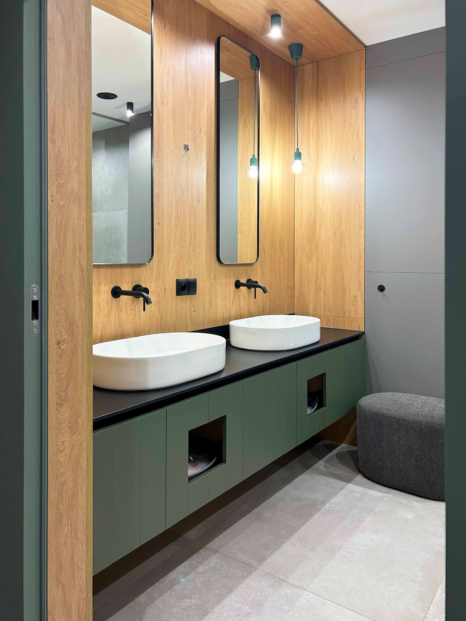 Nowoczesna łazienka z dwiema owalnymi umywalkami nablatowymi, czarną armaturą, szafką w odcieniach zieleni, drewnianą boazerią na ścianie i wiszącymi lampami z żarówkami edisona.