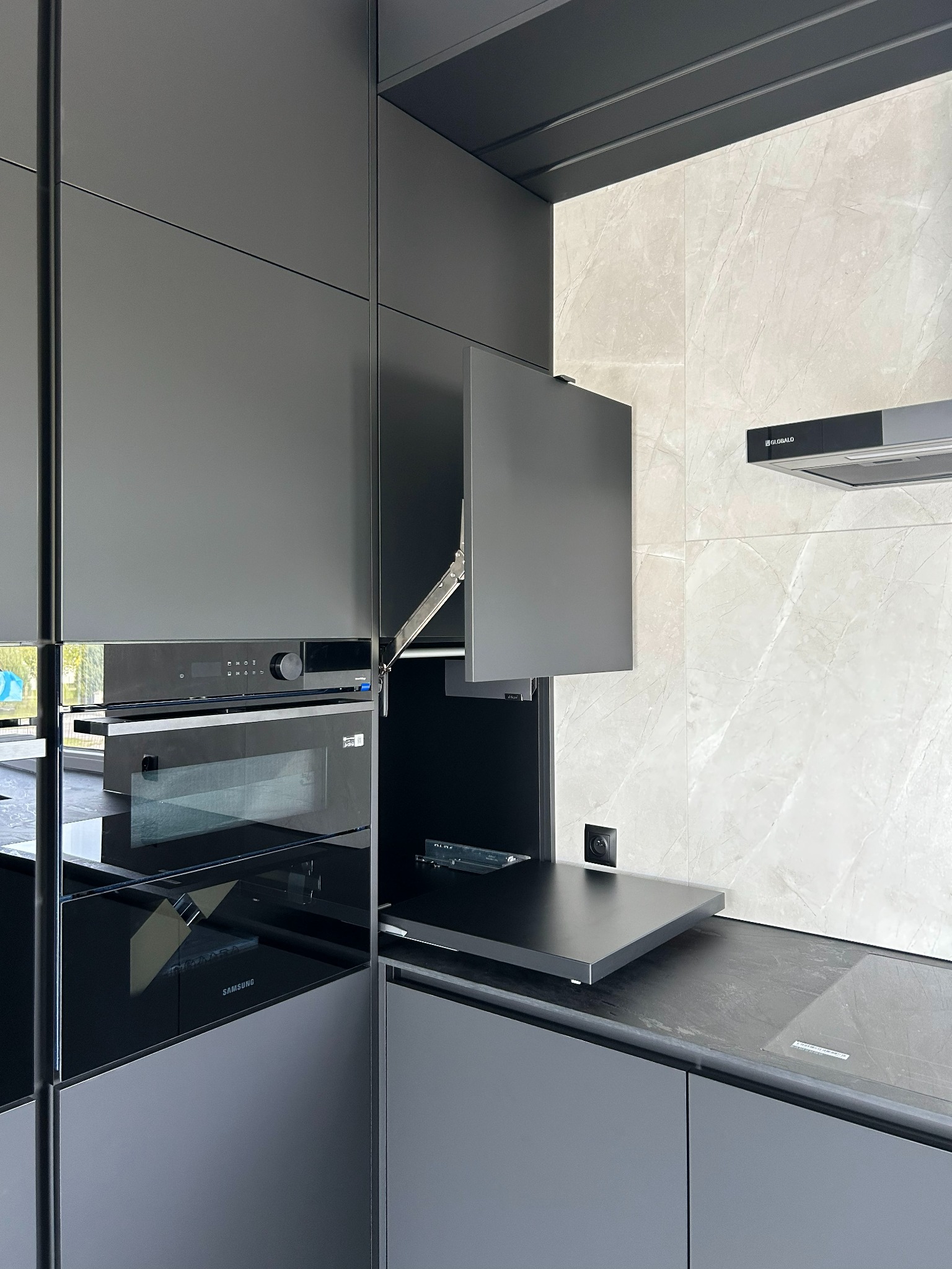 Nowoczesna, matowa kuchnia na wymiar w odcieniach szarości z otwartą szafką i piekarnikiem Samsung, zrealizowana w Łańcucie. Minimalistyczny design i funkcjonalność.