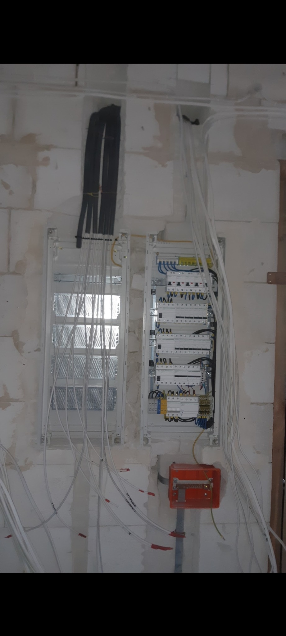 Dwa rozdzielnice elektryczne w trakcie instalacji w Skierniewicach, z widocznymi przewodami, zamontowane na surowej ścianie z betonu komórkowego.