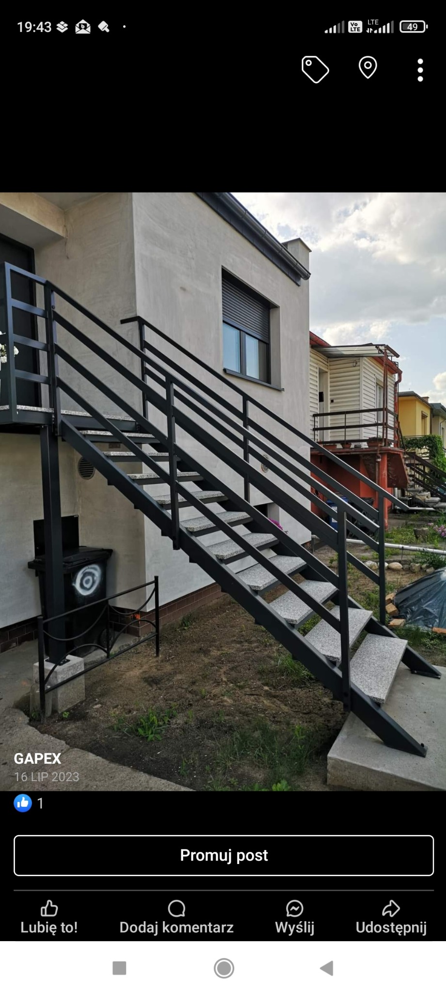 Zewnętrzne schody z czarnej stali z szarymi stopniami prowadzące do wejścia do budynku, obok śmietnika z graffiti.