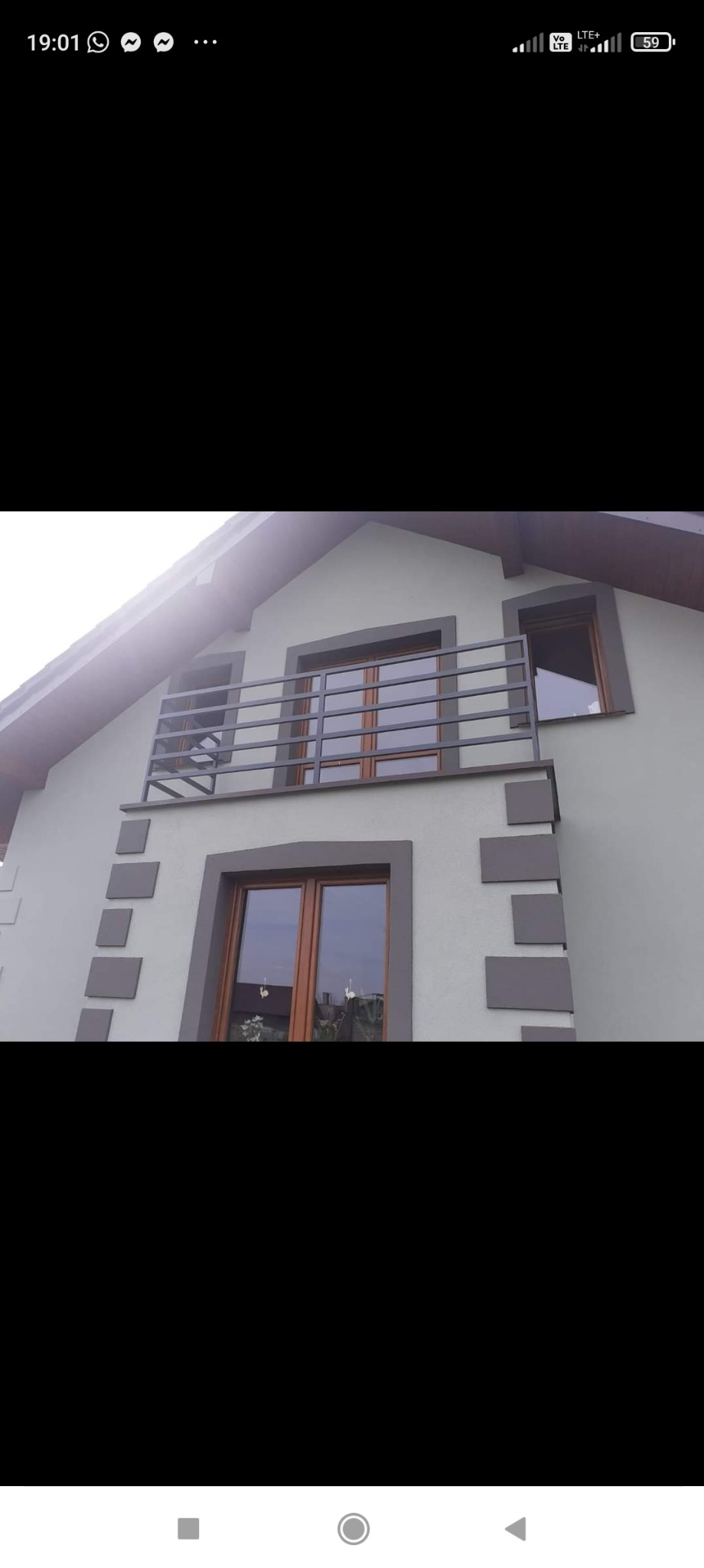 Szary dom jednorodzinny z balkonem zabezpieczonym prostą, poziomą, metalową konstrukcją, widoczne okna z brązowymi ramami i dekoracyjne szare kwadraty na elewacji.