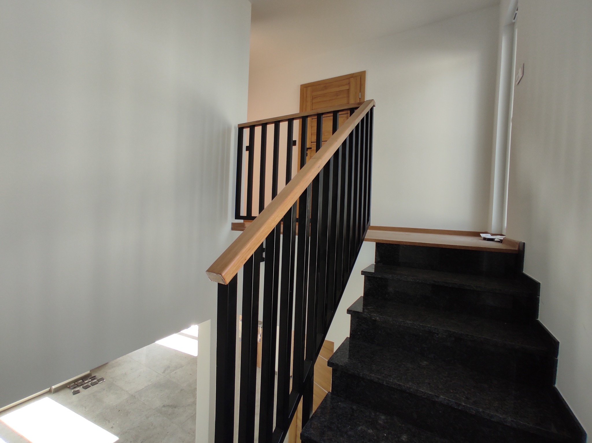 Granitowe schody z czarną metalową balustradą i drewnianym poręczą, widok z góry na dół, w tle drzwi.