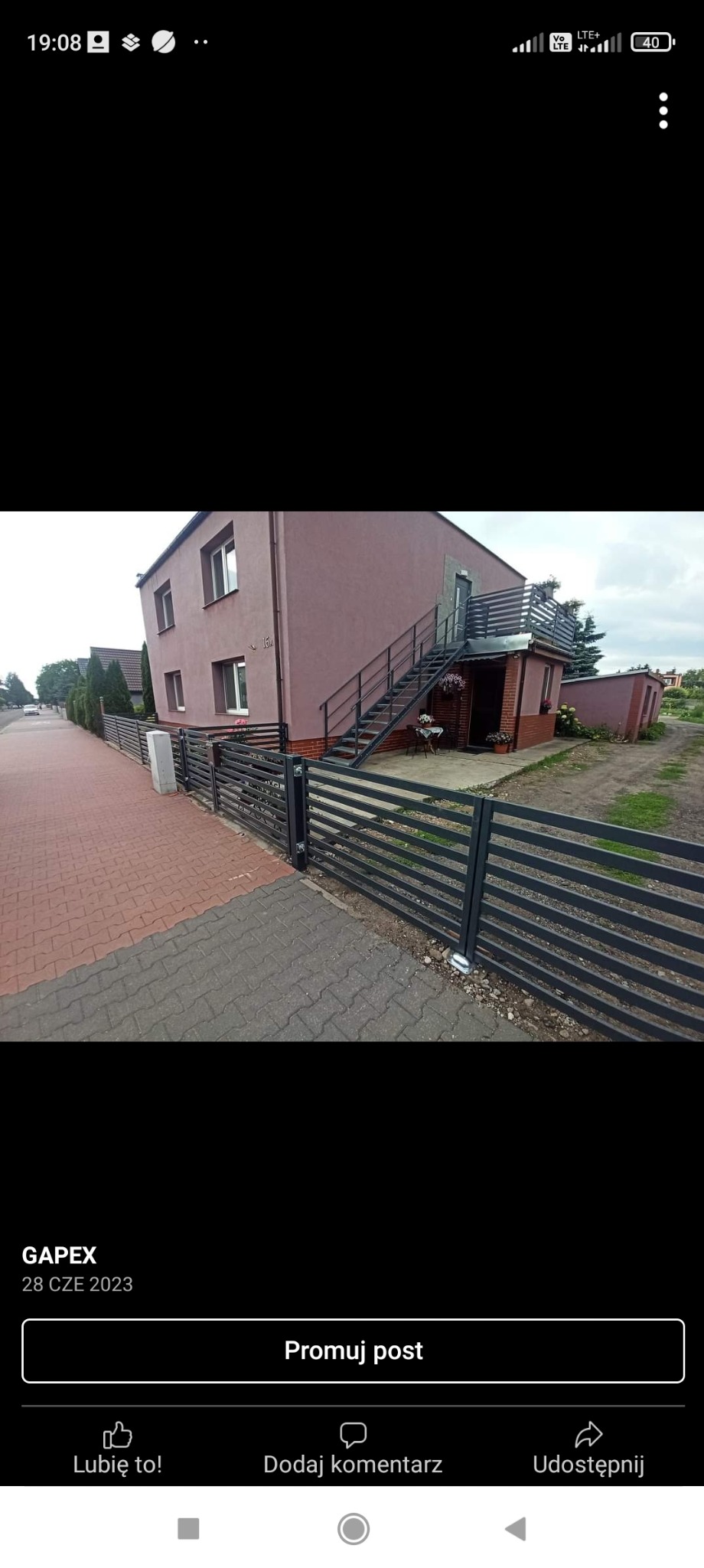 Nowoczesne ogrodzenie posesji z poziomych, szarych profili metalowych, dopasowane do elewacji domu z zewnętrznymi schodami prowadzącymi na balkon.