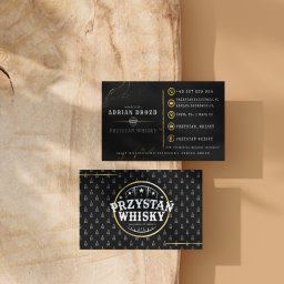 SzelixMedia Julia Szelerska - Dwie wizytówki firmy 'Przystań Whisky' na drewnianym tle, prezentujące logo, dane kontaktowe i wzór z małymi butelkami whisky.