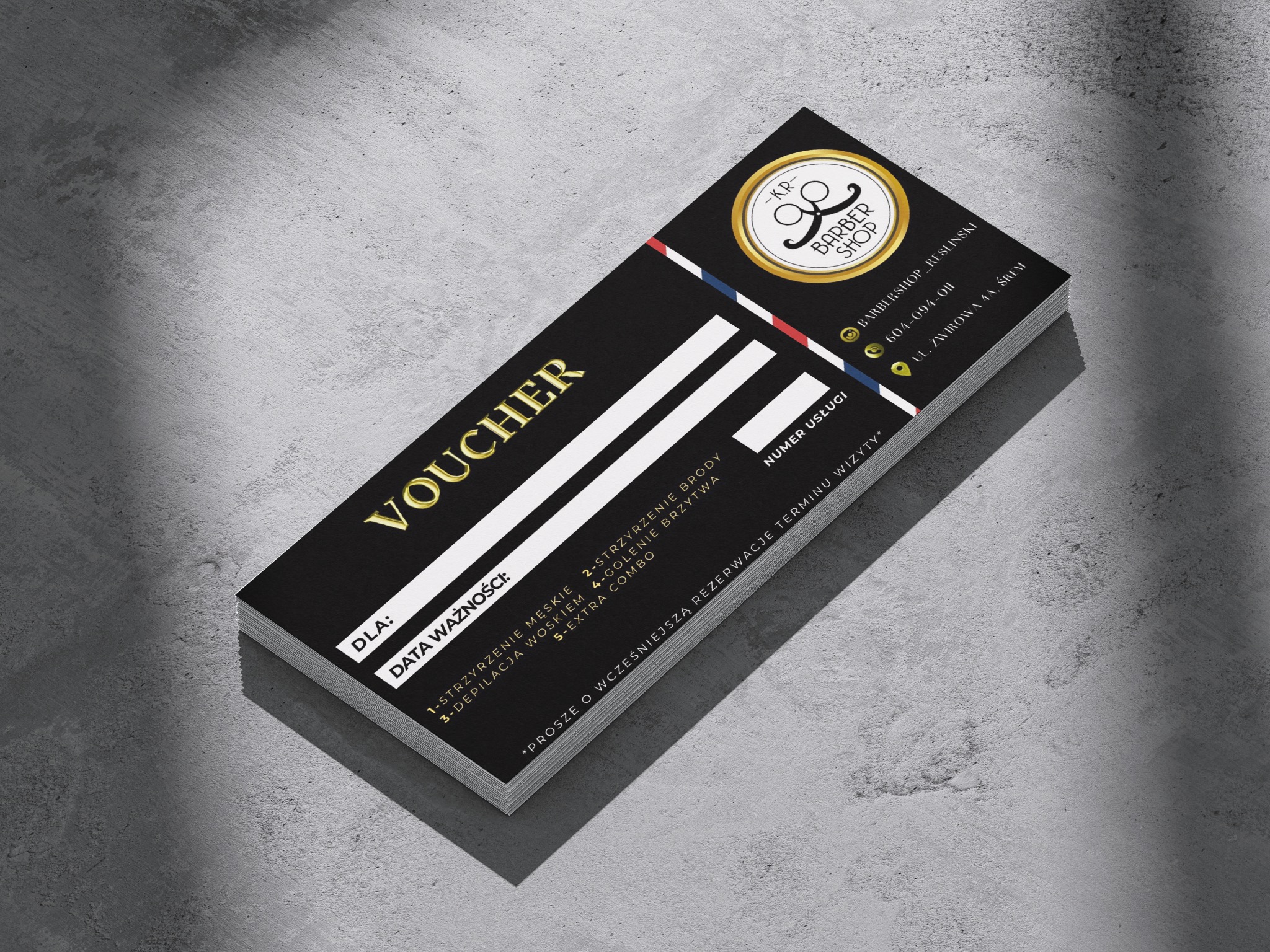 Czarny voucher z elementami złota dla barber shopu z logo, danymi kontaktowymi i listą usług, leżący na szarym tle.