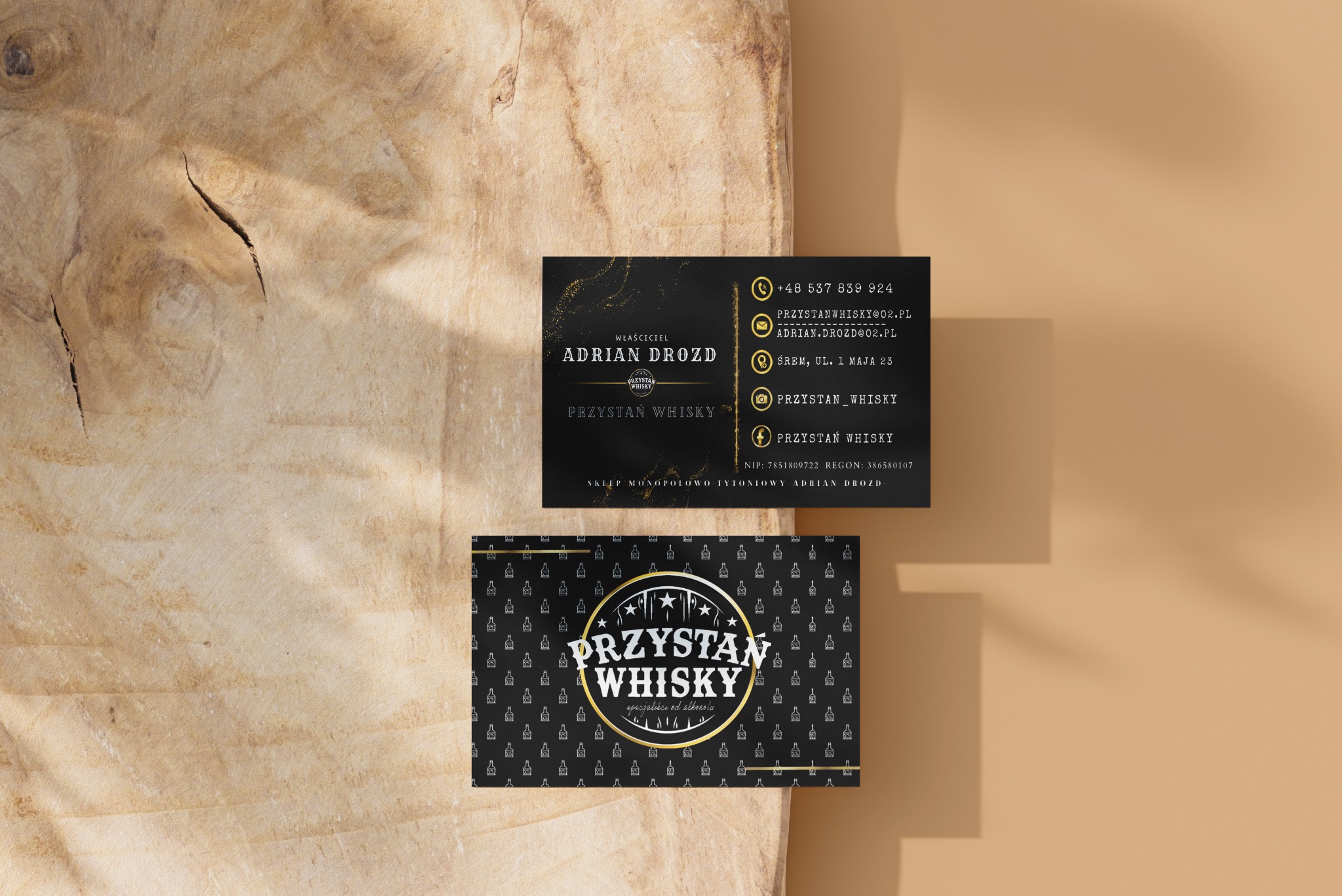 Dwie wizytówki firmy 'Przystań Whisky' na drewnianym tle, prezentujące logo, dane kontaktowe i wzór z małymi butelkami whisky.