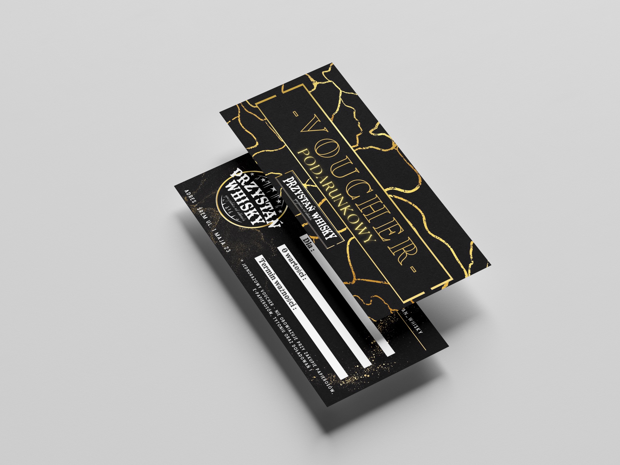 Dwa eleganckie, czarno-złote vouchery podarunkowe z nazwą 'Przystań Whisky', ułożone pod kątem na jasnoszarym tle, z widocznymi polami do wypełnienia wartości i terminu ważności.