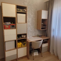 Rafał Kasprzyk - Pokój dziecięcy z biurkiem, krzesłem na złotych nóżkach i regałem z półkami oraz szafką wiszącą, oświetlony lampą sufitową z białymi kulami.