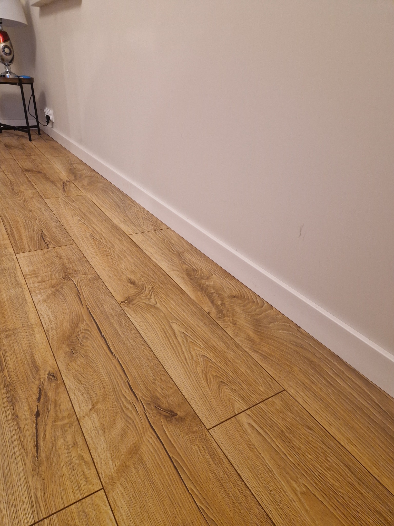 Ułożona podłoga z paneli imitujących drewno, widoczna listwa przypodłogowa i fragment ściany w jasnym odcieniu.