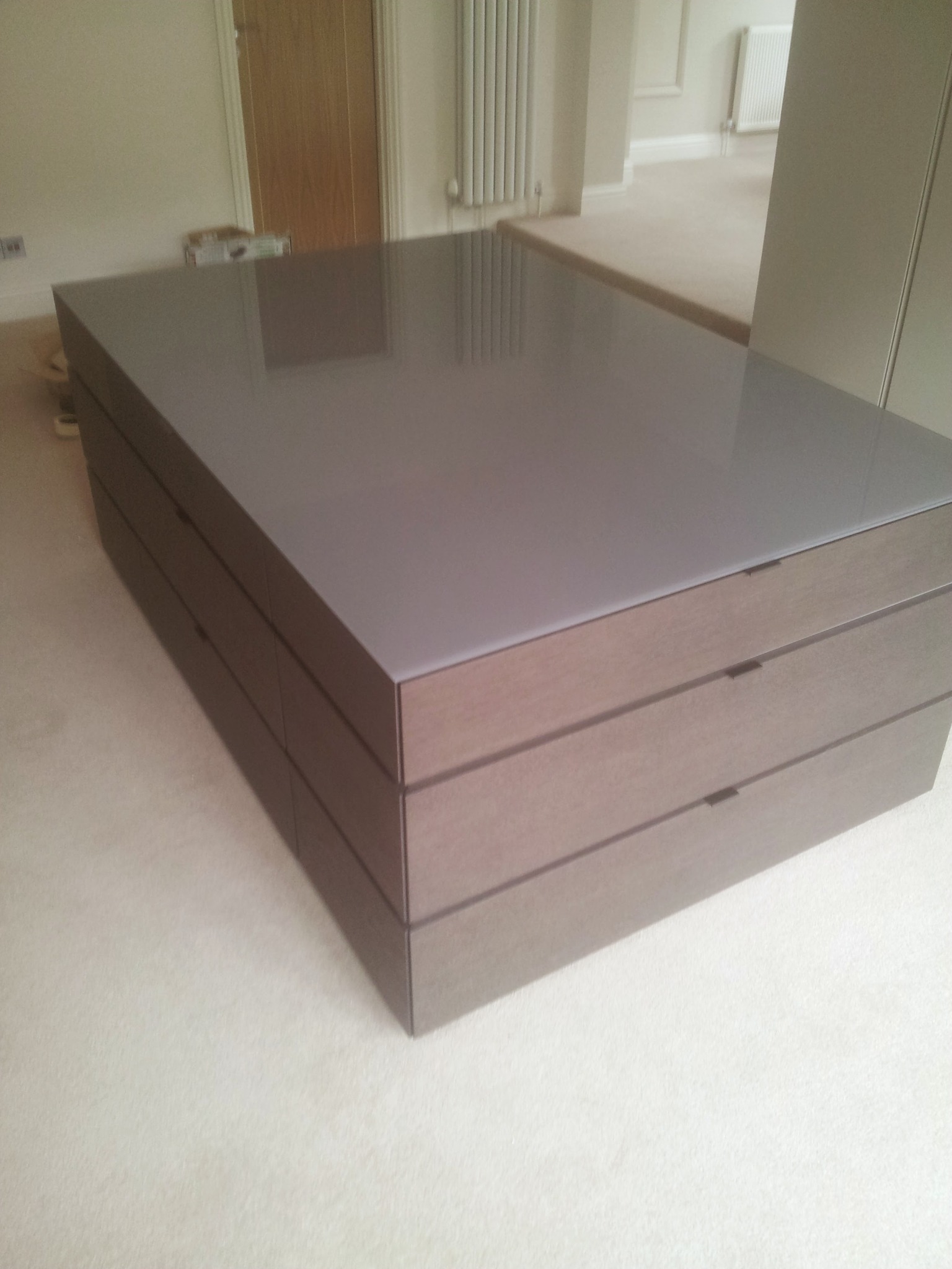 Niska komoda z szufladami, wykończona drewnem i szarym blatem, ustawiona na beżowej wykładzinie w jasnym wnętrzu.