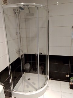 Półokrągła kabina prysznicowa z chromowanymi elementami i brodzikiem, wyłożona białymi i czarnymi płytkami ceramicznymi, widok z boku.