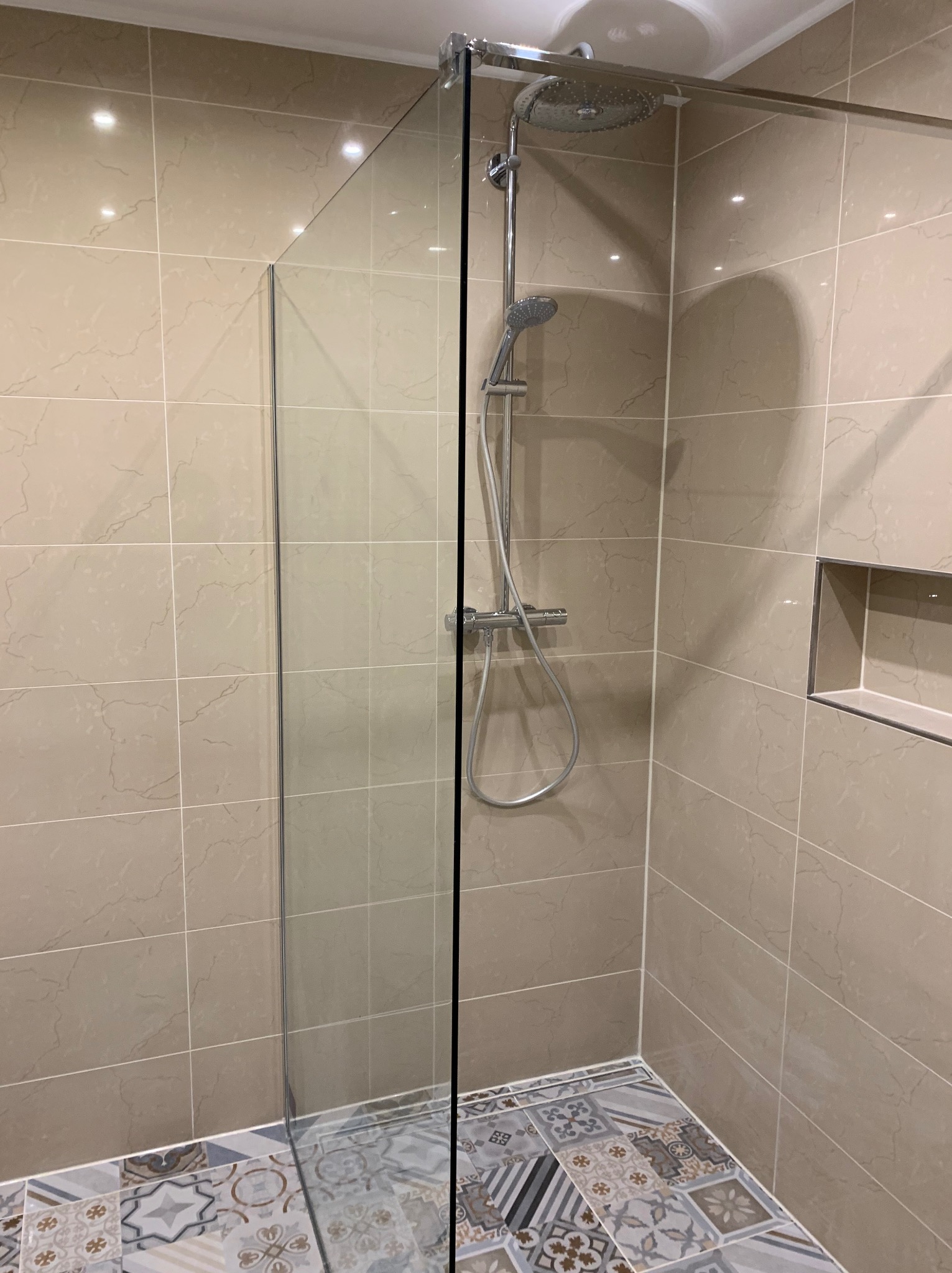 Kabina prysznicowa typu walk-in z chromowaną armaturą i deszczownicą, beżowe płytki ścienne imitujące marmur, dekoracyjna mozaika podłogowa z motywami geometrycznymi i kwiatowymi, wnęka ścienna...