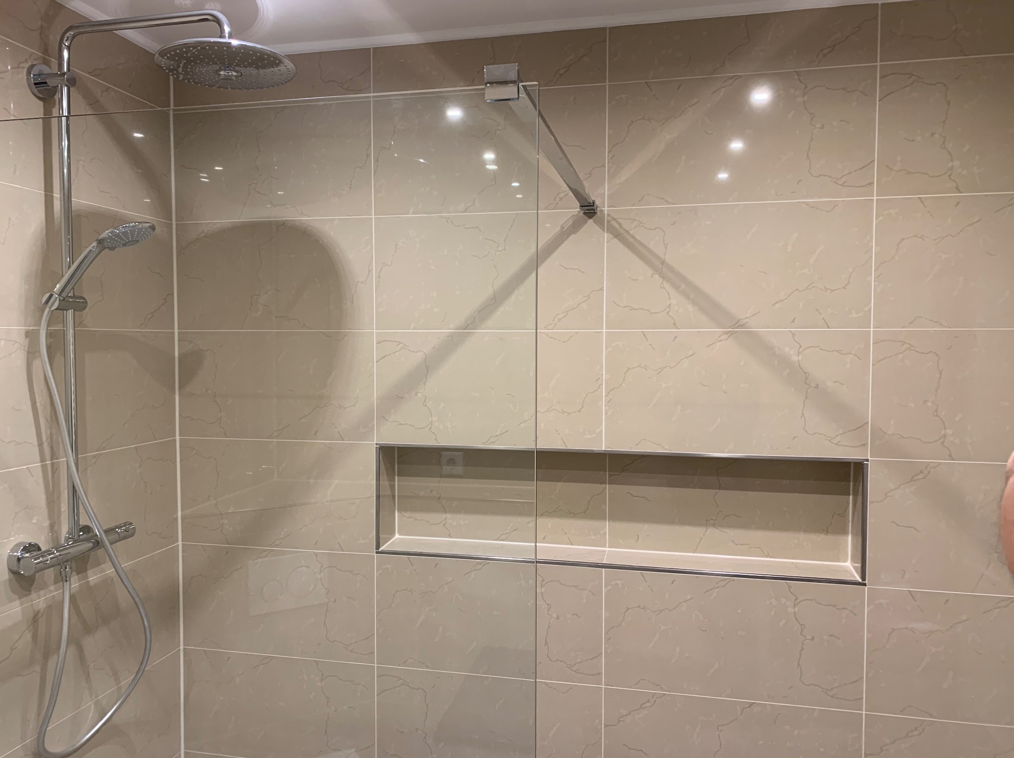 Beżowa łazienka w Toruniu z kabiną prysznicową typu walk-in, deszczownicą i półką w ścianie wyłożonej płytkami imitującymi marmur.