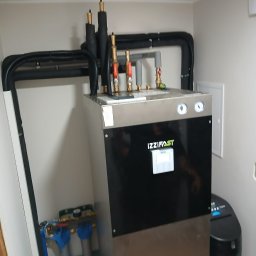 Grupa Majewscy Sp. Z O.O. - Nowoczesny piec Izzifast z kompletną instalacją hydrauliczną i rurami w izolacji, zamontowany w pomieszczeniu. Widoczne filtry i zawory.