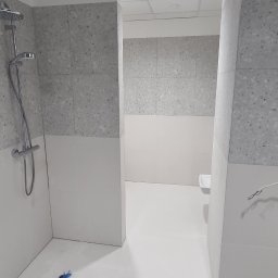 ŁYSZYK GROUP SPÓŁKA Z OGRANICZONĄ ODPOWIEDZIALNOŚCIĄ - Wykończona łazienka z szarymi płytkami imitującymi lastryko w strefie prysznica i nad umywalką, białe płytki na dolnej części ścian i podłodze, widoczny zestaw prysznicowy i niebieski element...