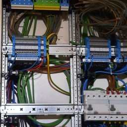 Elektro-S - Rozdzielnica elektryczna z widocznymi bezpiecznikami, listwami zaciskowymi i uporządkowanymi przewodami w różnych kolorach, zamontowana w metalowej obudowie.