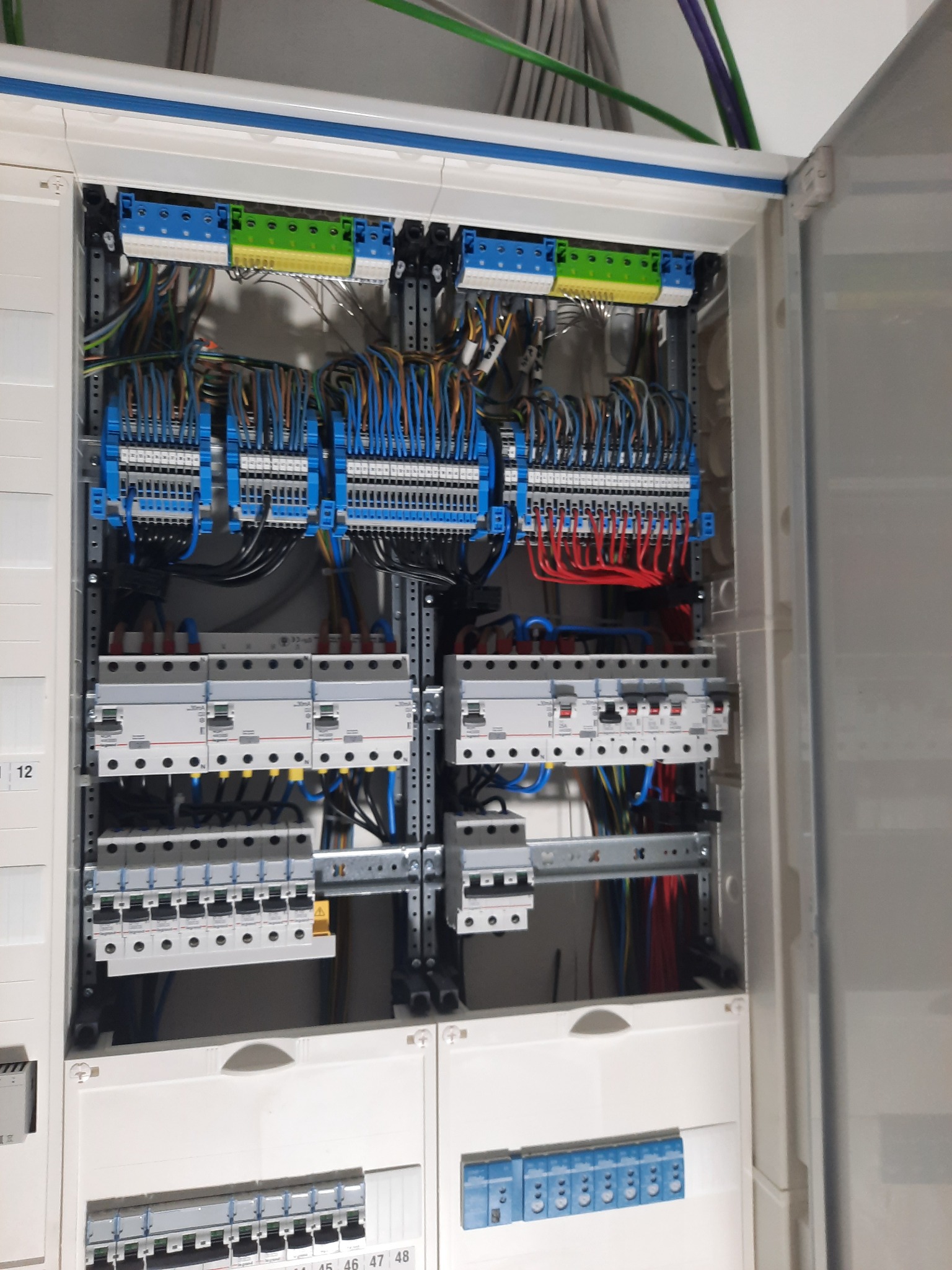 Otwarta szafa elektryczna z widocznymi bezpiecznikami, listwami zaciskowymi i przewodami w różnych kolorach, uporządkowanymi wewnątrz obudowy.