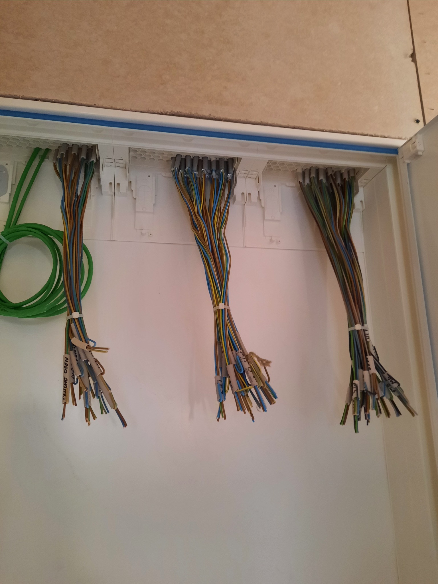 Rozdzielnia elektryczna z trzema wiązkami przewodów oznaczonych etykietami, z widocznymi żyłami i zielonym przewodem ułożonym w pętlę.