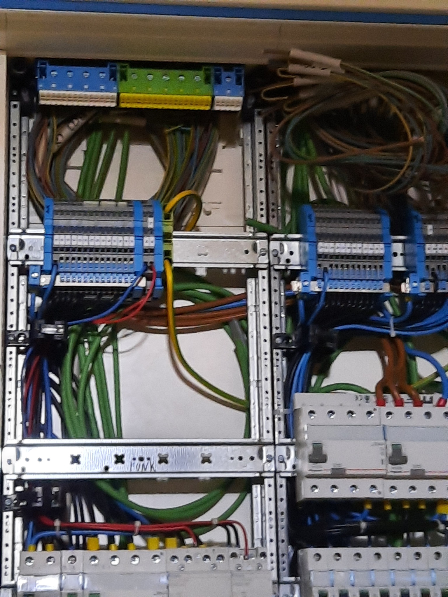 Rozdzielnica elektryczna z widocznymi bezpiecznikami, listwami zaciskowymi i uporządkowanymi przewodami w różnych kolorach, zamontowana w metalowej obudowie.