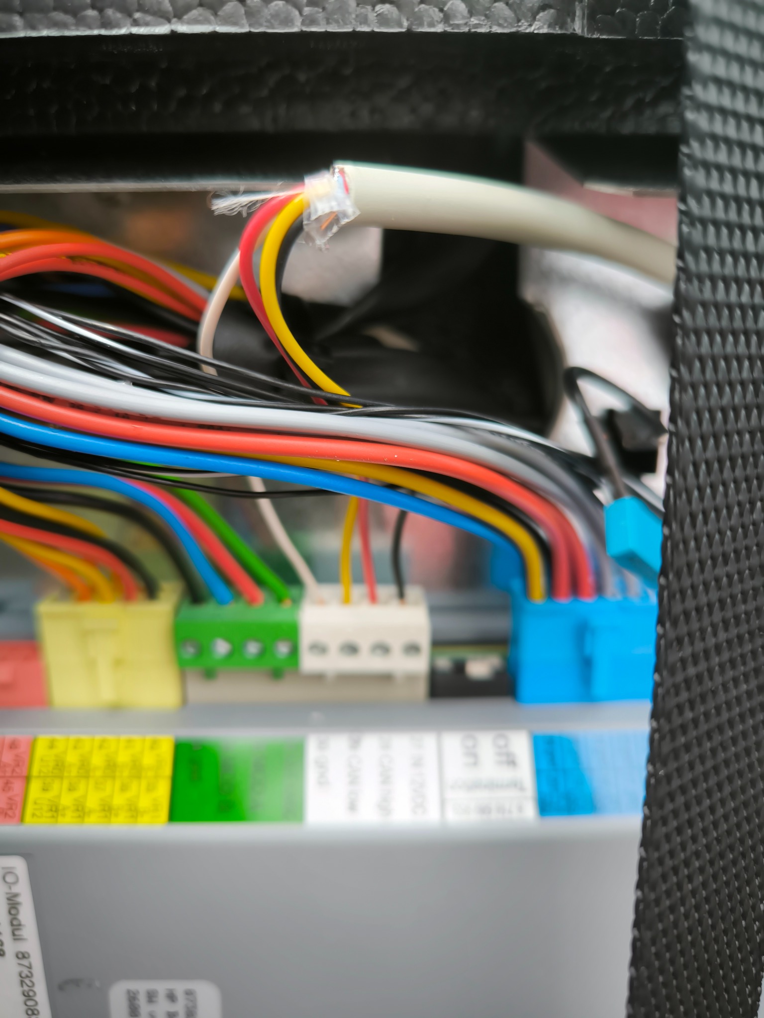 Szczegółowe zbliżenie na podłączenie wielokolorowych przewodów do listwy zaciskowej wewnątrz skrzynki sterowniczej, widoczne oznaczenia na module I/O.