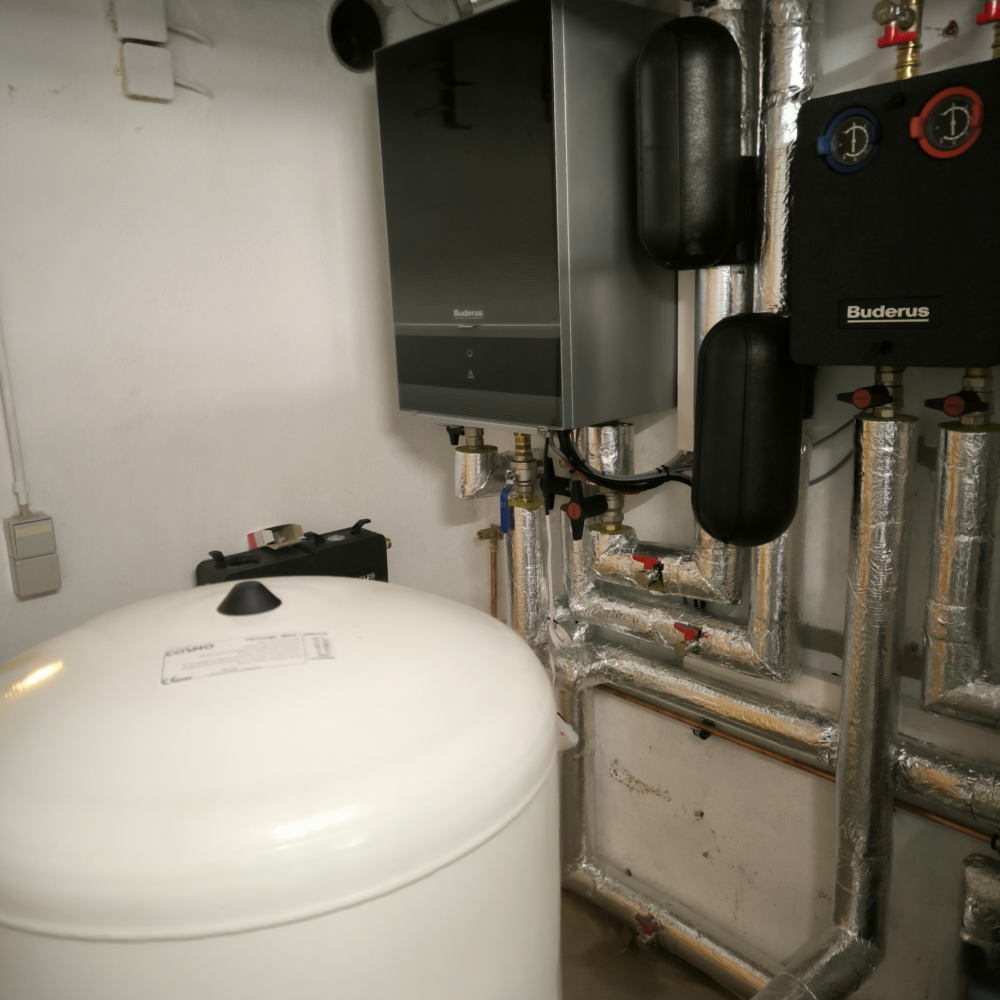 Kotłownia z zamontowanym piecem gazowym Buderus, zasobnikiem ciepłej wody Cosmo i izolowanymi rurami.