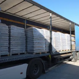 Ciężarówka z naczepą załadowana paletami z workami pelletu, zabezpieczonymi folią stretch, widoczne niebieskie niebo w tle.