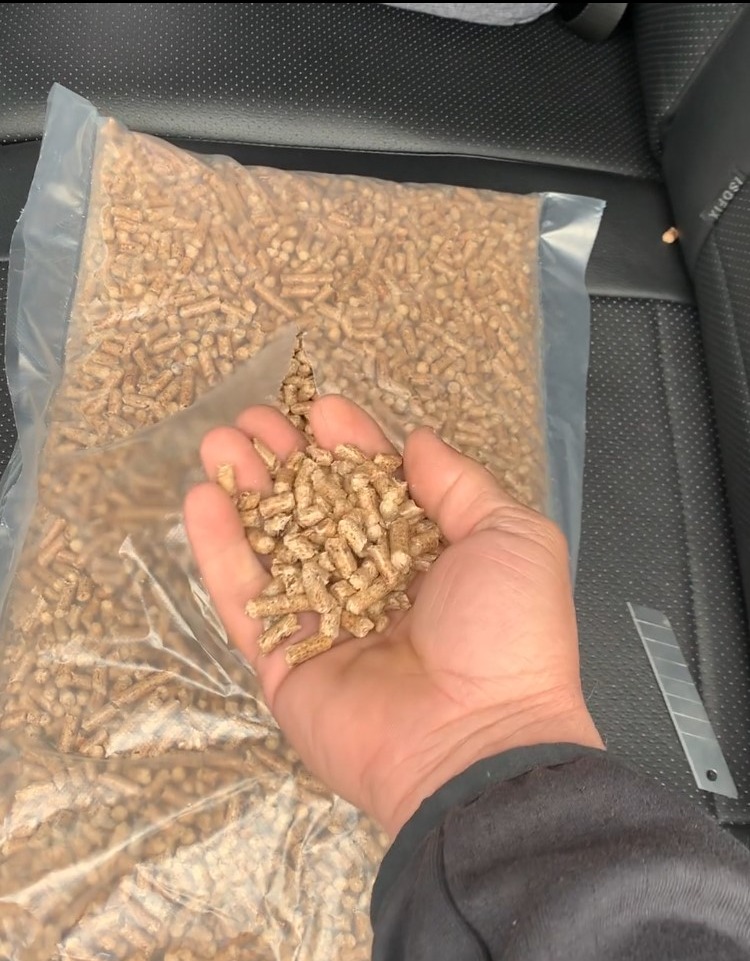 Dłoń trzyma garść pelletu na tle worka z pelletem, widoczny nóż introligatorski na siedzeniu samochodowym.