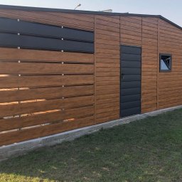 STYLMETAL Dawid Załubski - Nowoczesny garaż z drewnianą elewacją i metalowymi akcentami, zintegrowany z ogrodzeniem o poziomym układzie desek, osadzony na betonowej podmurówce na tle zielonego trawnika.
