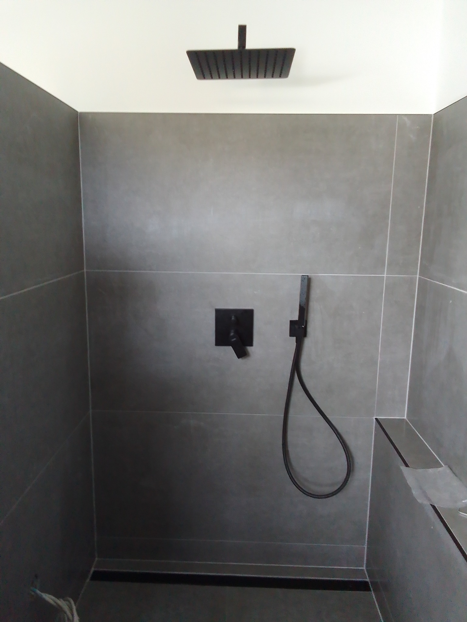 Nowoczesny prysznic z szarymi płytkami, czarną armaturą i deszczownicą, minimalistyczny design.