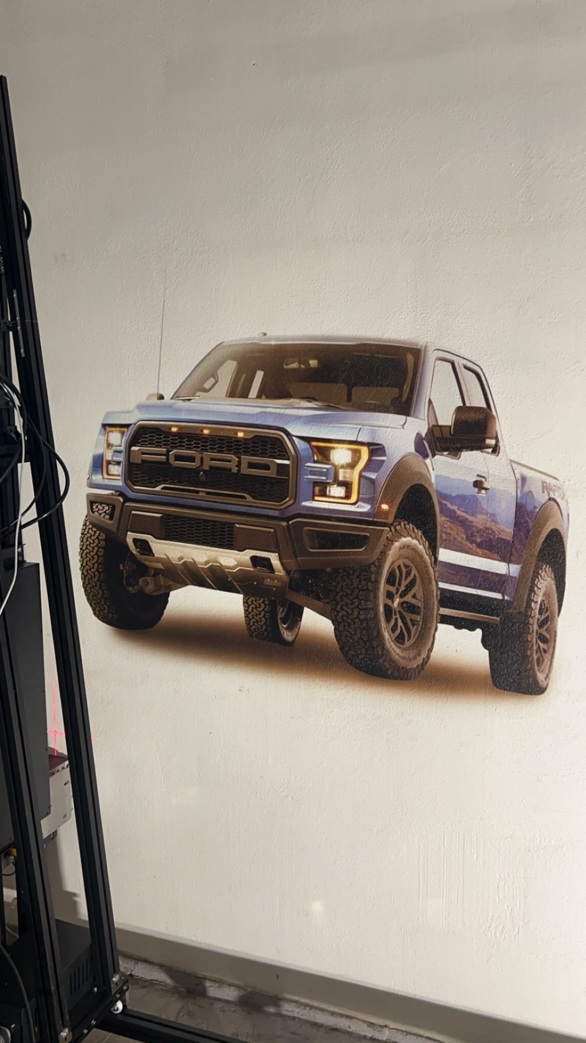 Niebieski Ford Raptor, wydrukowany na tapecie, widoczny z niskiej perspektywy, z fragmentem czarnej ramy drukarki po lewej stronie.