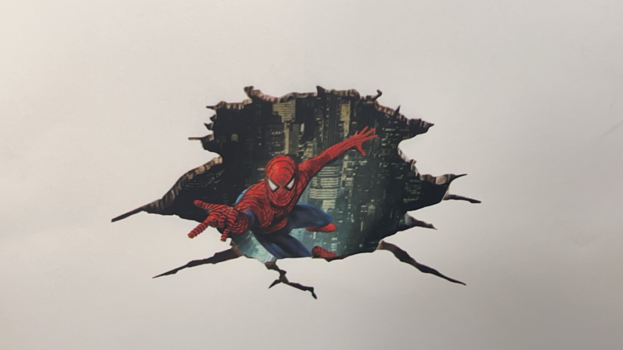 Naklejka ścienna z motywem Spider-Mana przebijającego się przez ścianę, widok na miasto w tle.