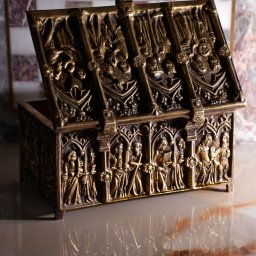 Wiktoria Żółciak - Otwarta, zdobiona, metalowa szkatułka z reliefami postaci na marmurowym blacie, odbijająca się w powierzchni.