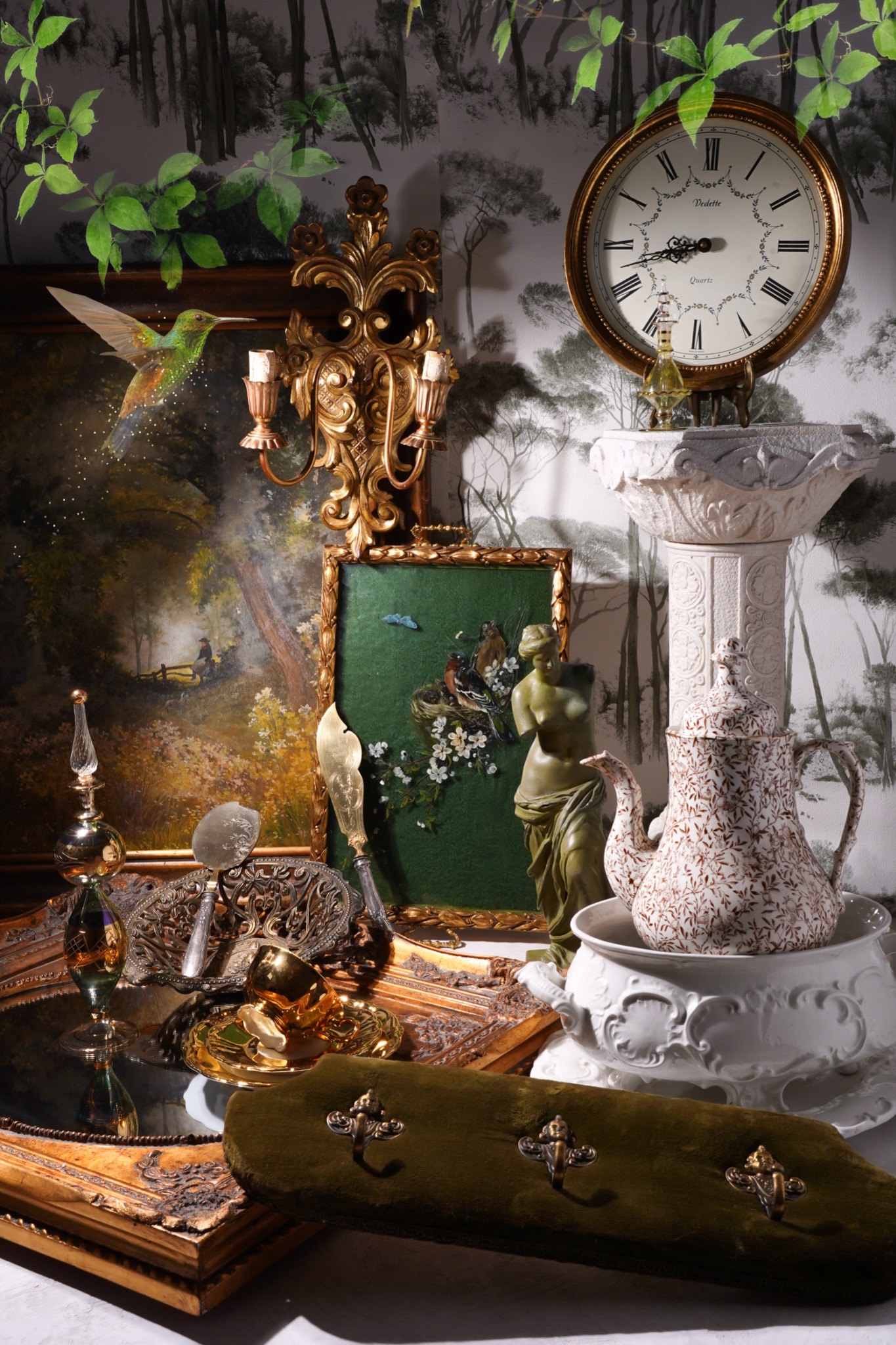 Martwa natura z antykami: zegar, obrazy, rzeźba, imbryk, lustrzana taca i wieszak na ubrania, na tle tapety z motywem leśnym.