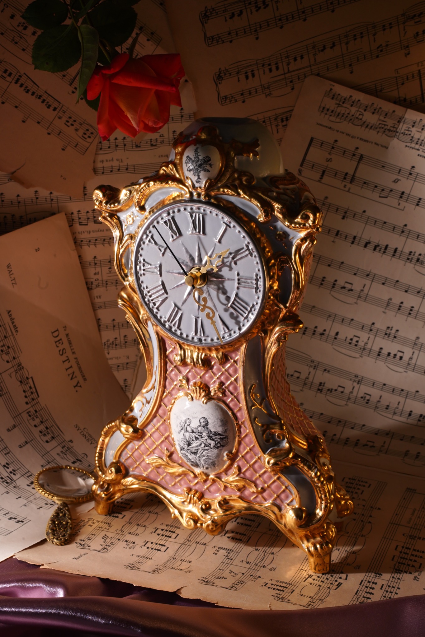 Dekoracyjny zegar kominkowy w stylu vintage z elementami złoconymi, ustawiony na tle starych nut i ozdobiony czerwoną różą, oświetlony ciepłym światłem.